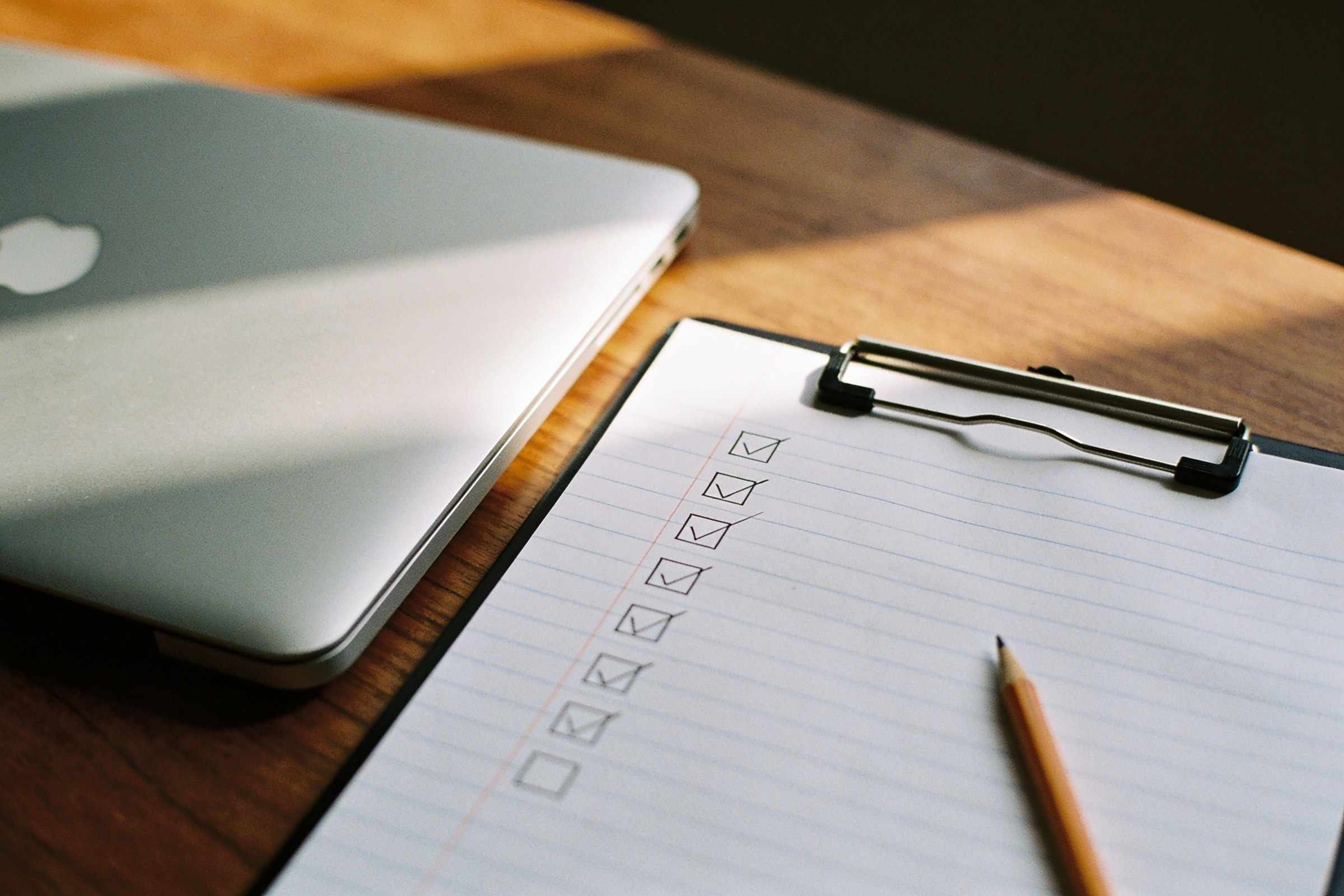 A printed checklist on a clipboard with most items ticked in pencil, next to a laptop.